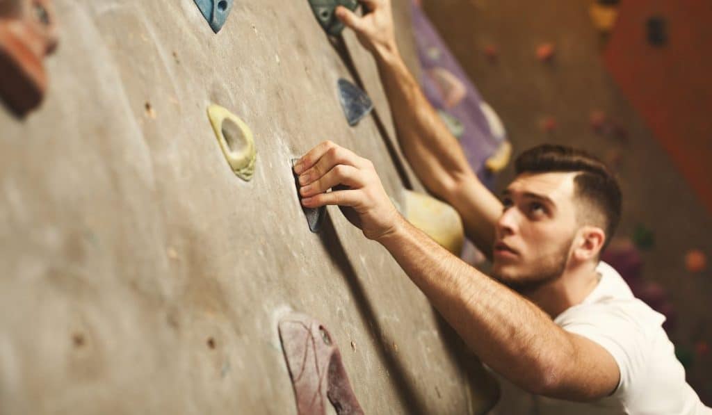 Young man practicing rock-climbing on artificial rock wall indoors