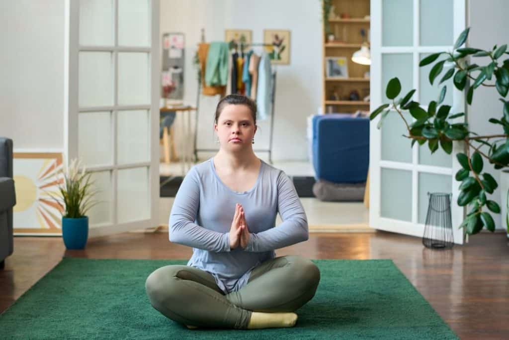 woman with disability sitting in pose of lotus on the floor living room, practicing yoga