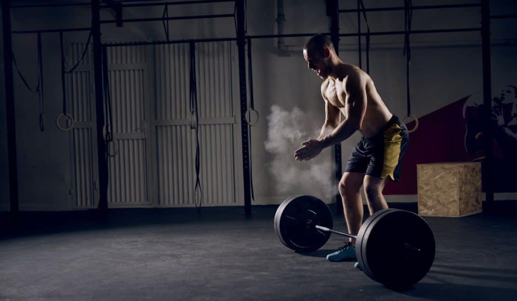 Athlete motivates screaming before barbells exercise at gym
