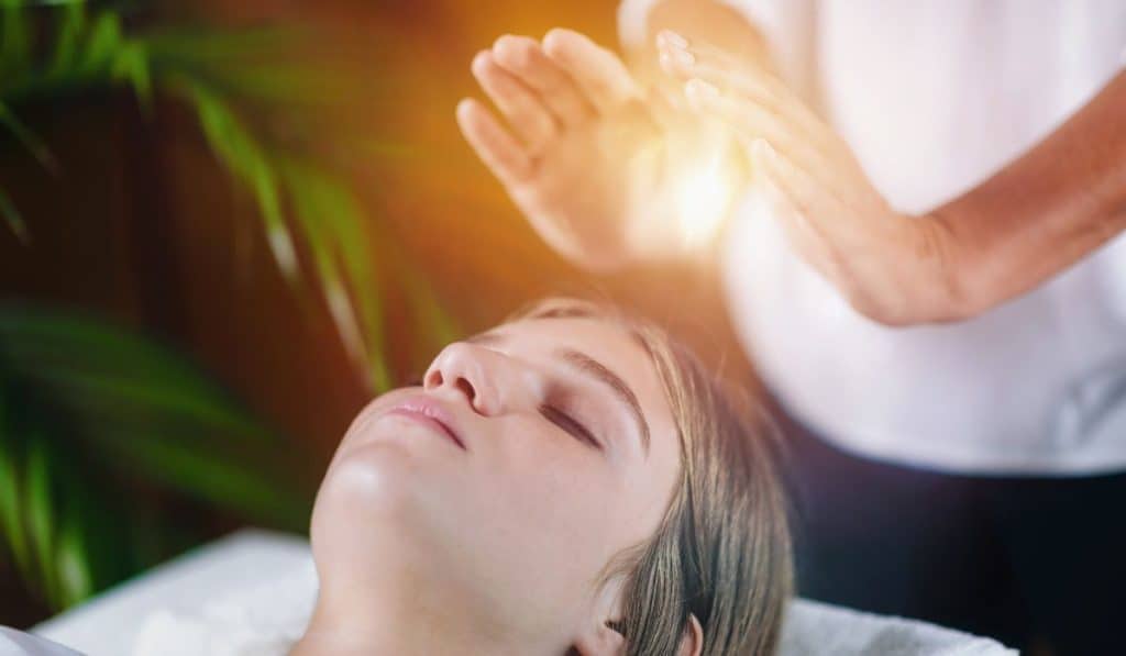 relaxed young woman lying with her eyes closed and having Reiki healing treatment