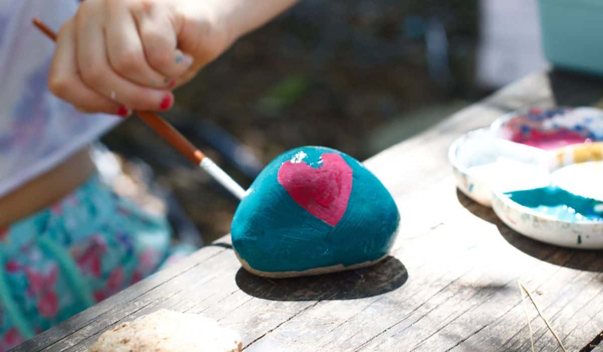 girl painting a pink heart on a colored blue stone