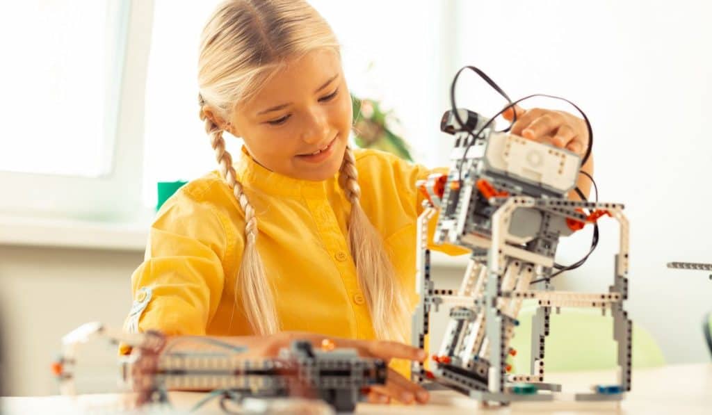 Cheerful girl sitting in the classroom playing with a robot she made at her school science lesson