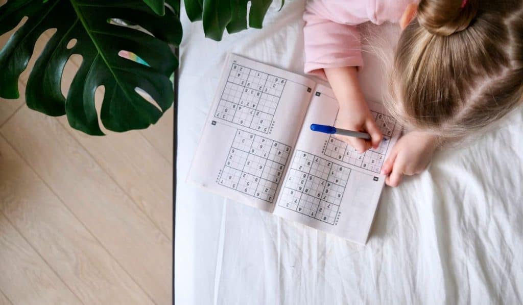 little girl playing in sudoku on her bed