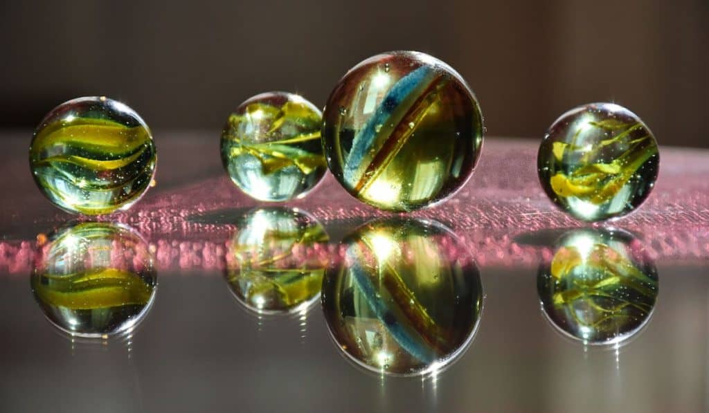 colorful children's glass marbles on a reflective glass surface
