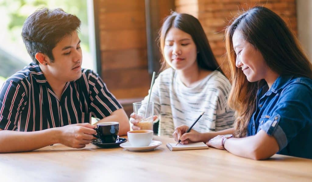 Group of friends writing down in a notebook while drinking coffee