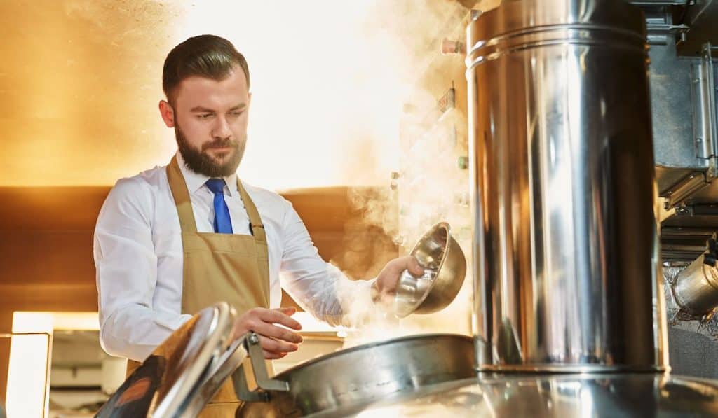 Professional brewer in white shirt and apron working in beer manufacturing factory