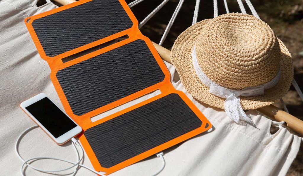 Smartphone is charging from solar battery lying in a hammock