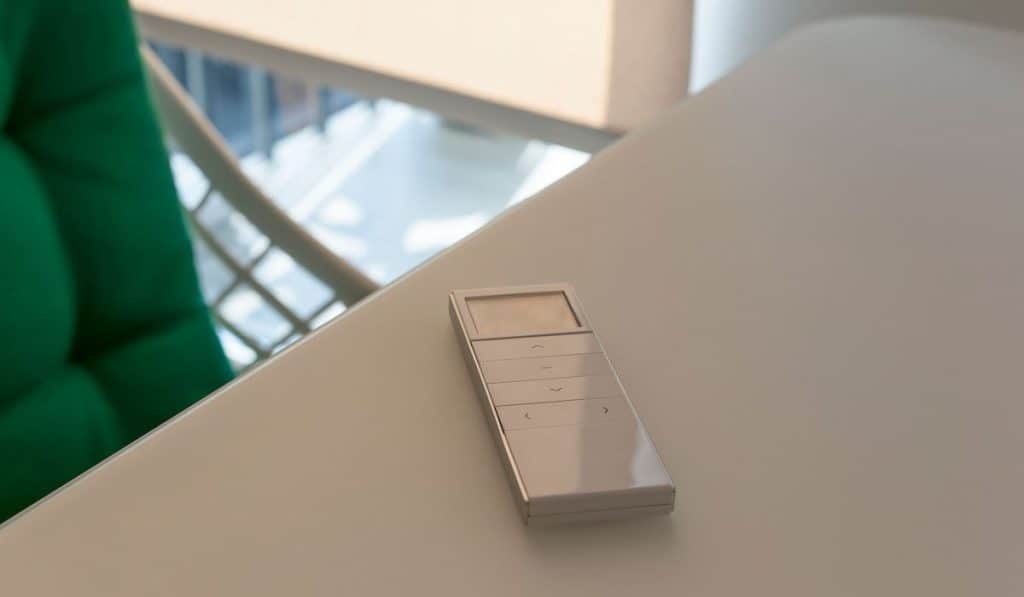 White remote control panel for automatic roller shades lies on a beige table in the living room