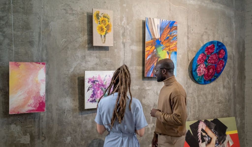 Young intercultural man and woman discussing one of paintings 