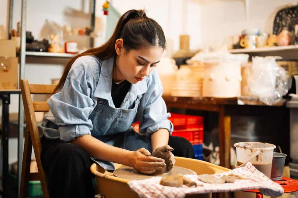 a pretty young woman making pots using clay in a workshop