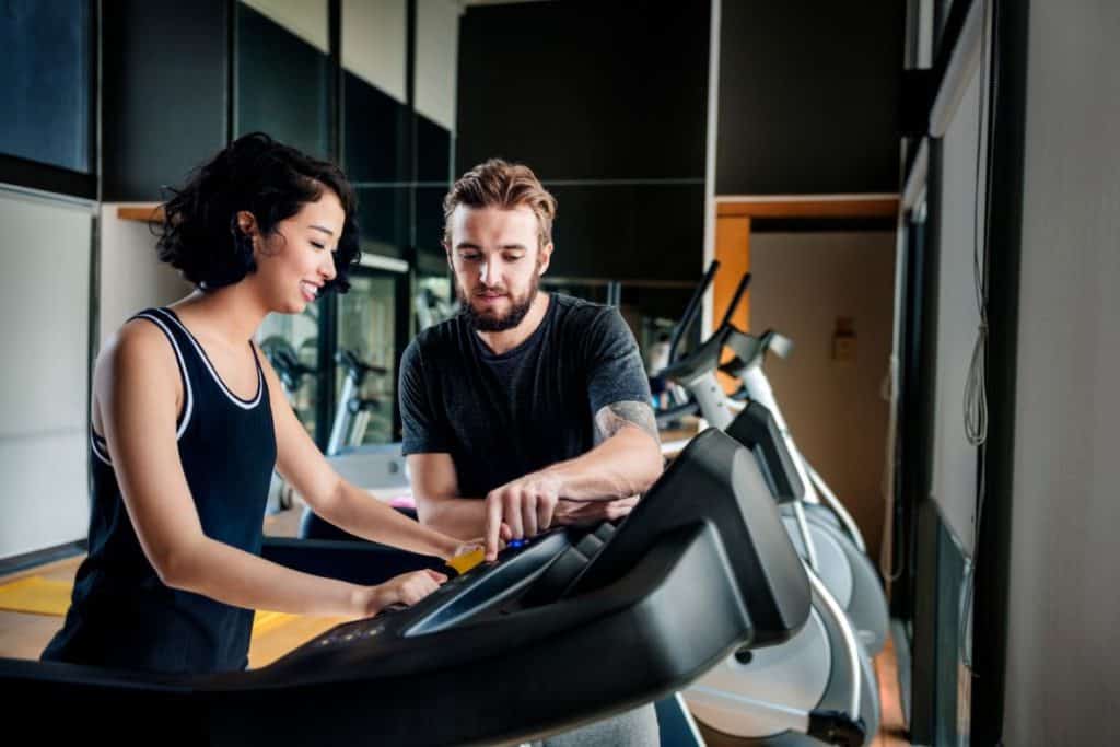 a woman doing her treadmill assisted by a fitness trainer in a gym