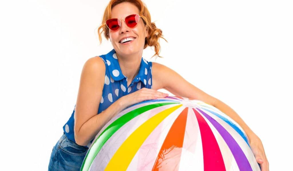 beautiful girl in sunglasses holds an inflatable big ball on a white background

