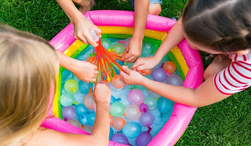 girls filling up water balloons at sunny day. Summer fun outdoor activities for children