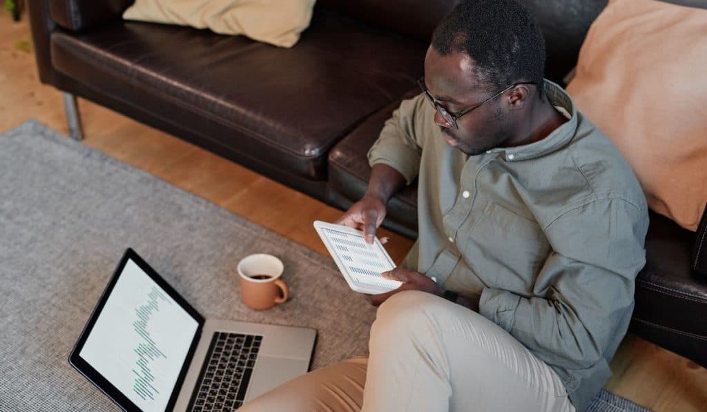 man sitting on floor in living room analysing stock trading graphs and charts