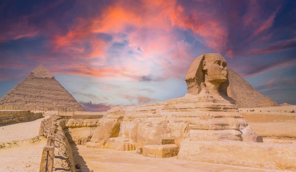 the Great Sphinx and the Pyramids of Giza against a colorful sunset at Giza