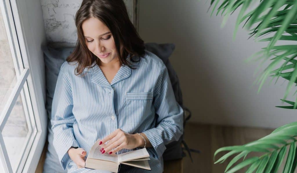 woman reading a book near windowsill at home