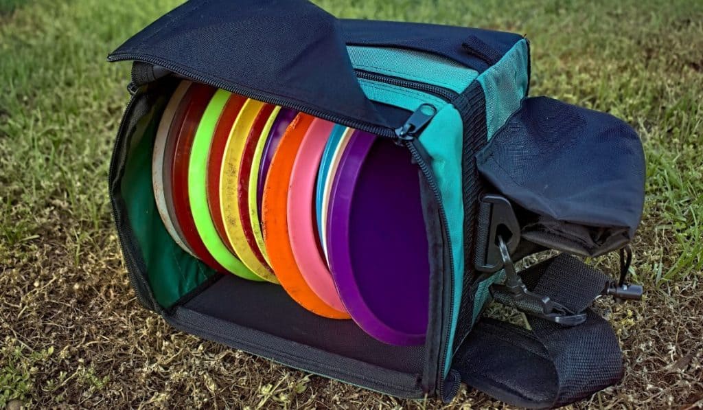 Bag of disc golf discs laying on grass.
