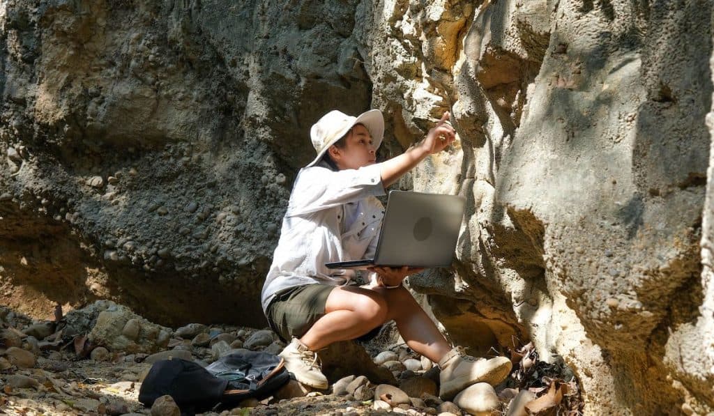 Female geologist using laptop computer examining nature, analyzing rocks or pebbles