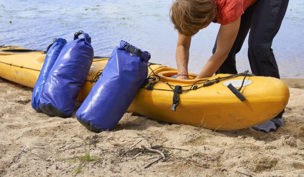 Female hiker inserting a waterproof bag with the things into the kayak
