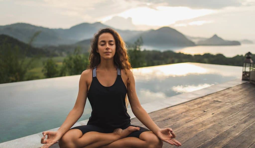 Young woman on meditation pose with pool and nature in background