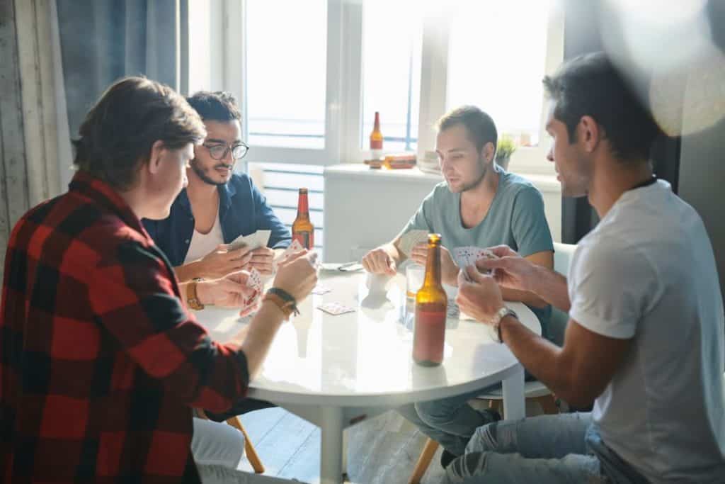 four men playing poker while drinking beer in the kitchen 