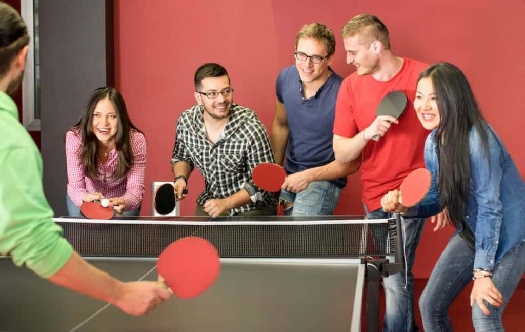 group of young friends surrounding a ping pong table for a relay 