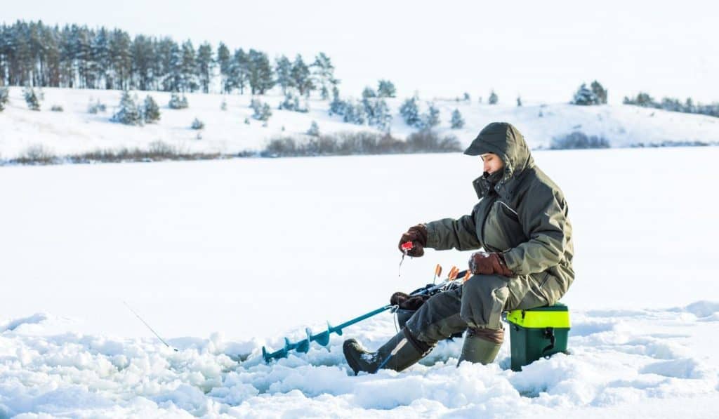 A young man is fishing from a hole on ice