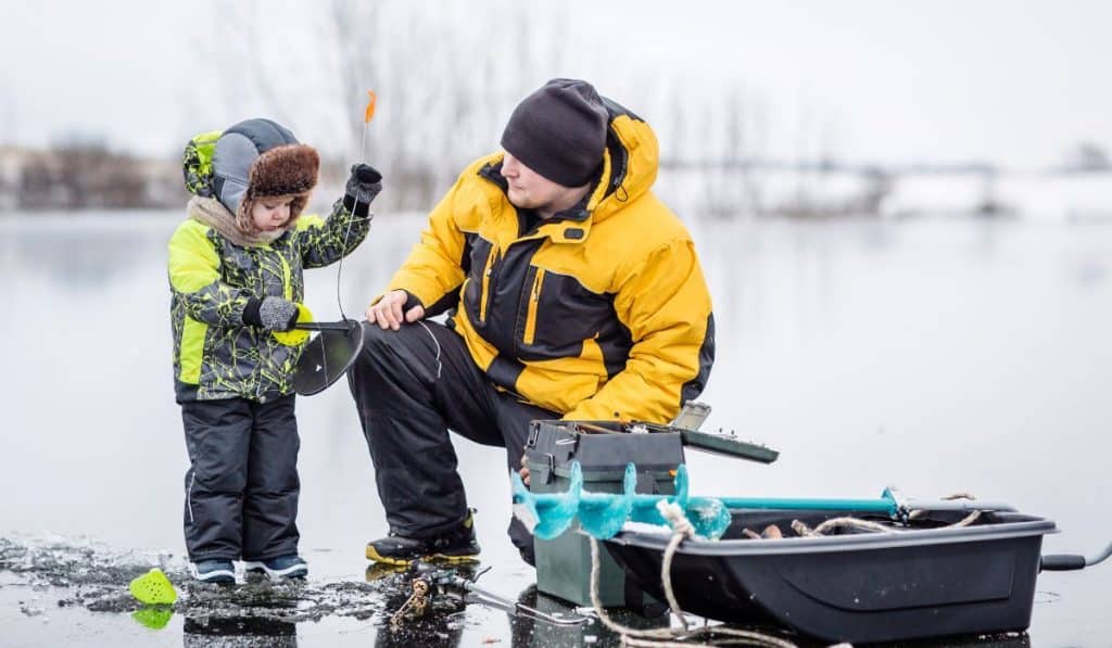 Father teaching his son how to fish on a frozen lake in winter.
