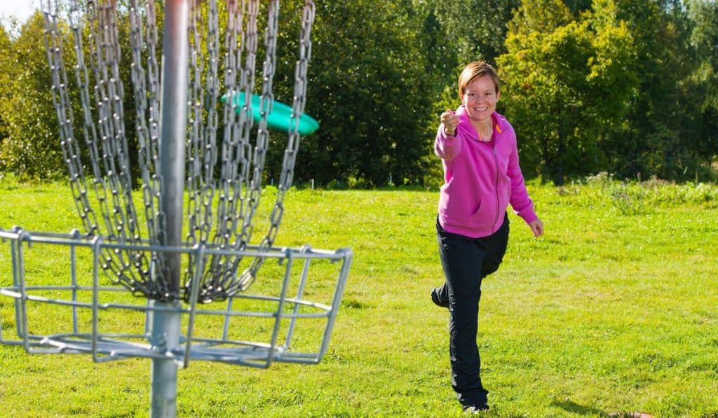 Woman throwing a disc to the disc basket

