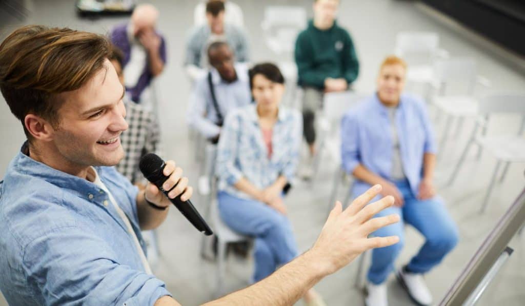 Man speaking using a microphone with audience in front of him