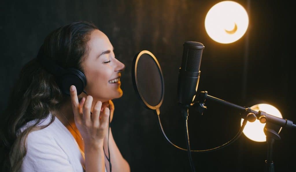 Young woman singer recording song using microphone in a studio