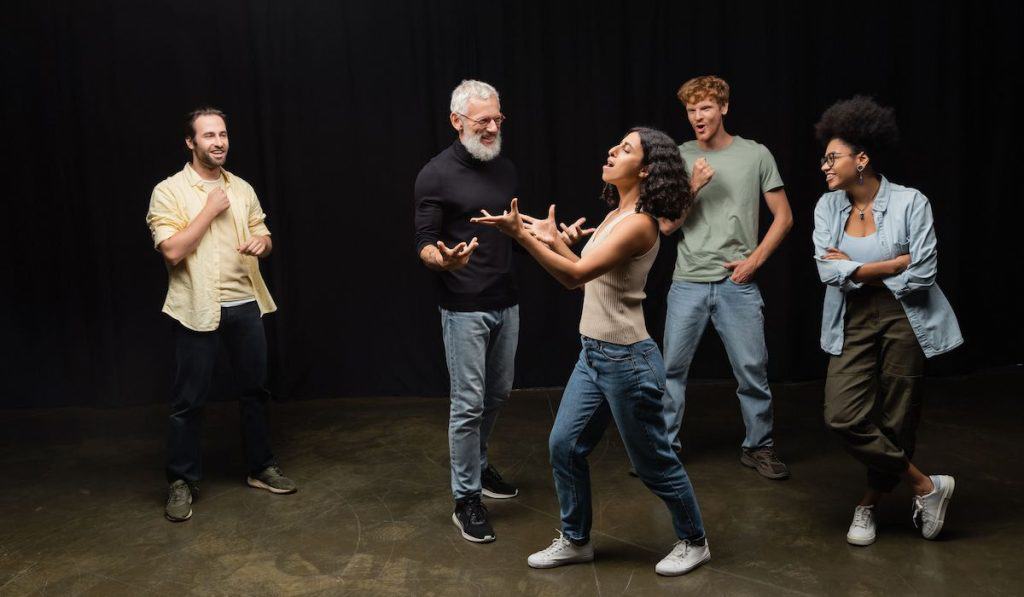 woman gesturing while rehearsing near bearded art director and smiling interracial actors