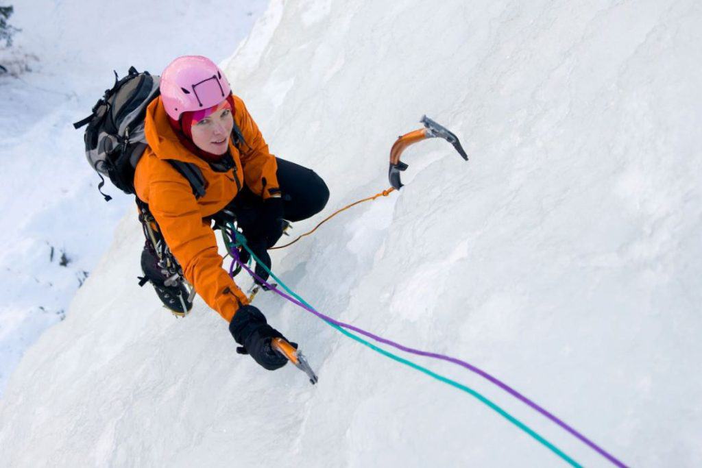 a woman in orange jacket climbing ice wall