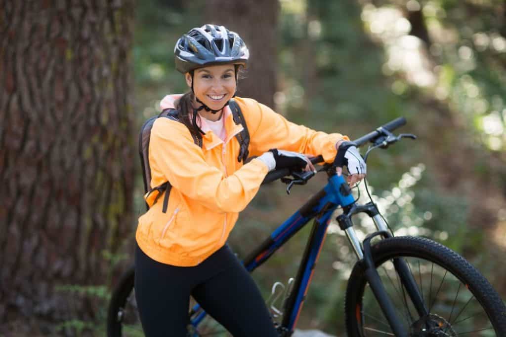 female biker standing with mountain bike in forest at countryside