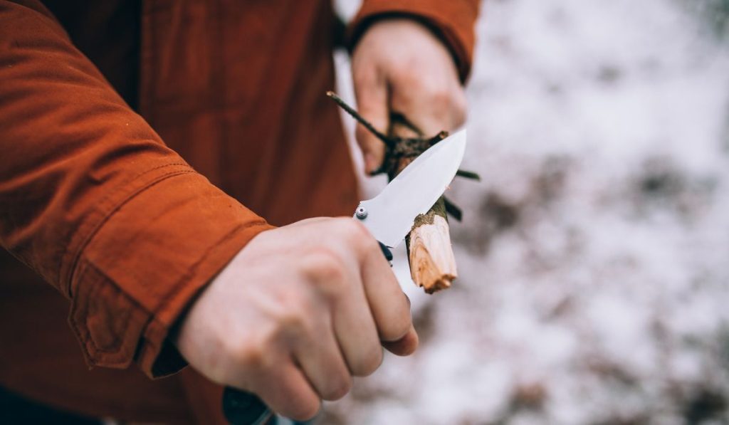 A man uses a knife to whittle a stick out hiking
