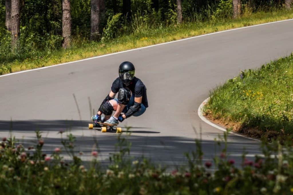 A man wearing a black shirt and helmet doing street luge with a long board