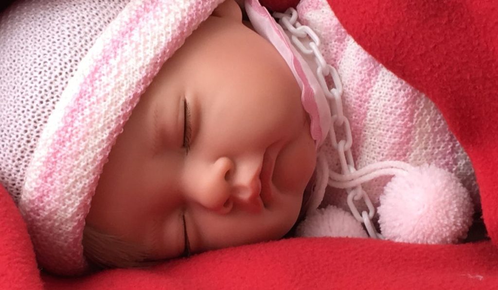 Baby doll with cap sleeping and wrapped in blanket.