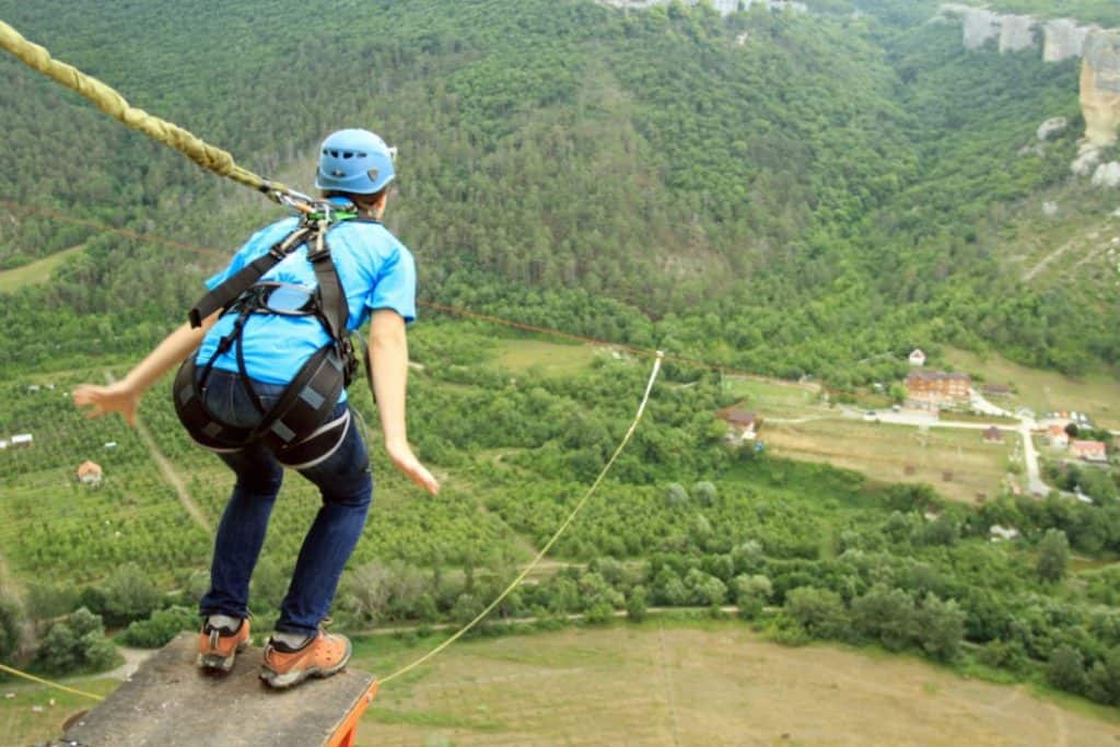 a girl in blue shirt and helmet about to jump from the cliff