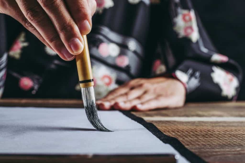 a woman in kimono doing Japanese calligraphy