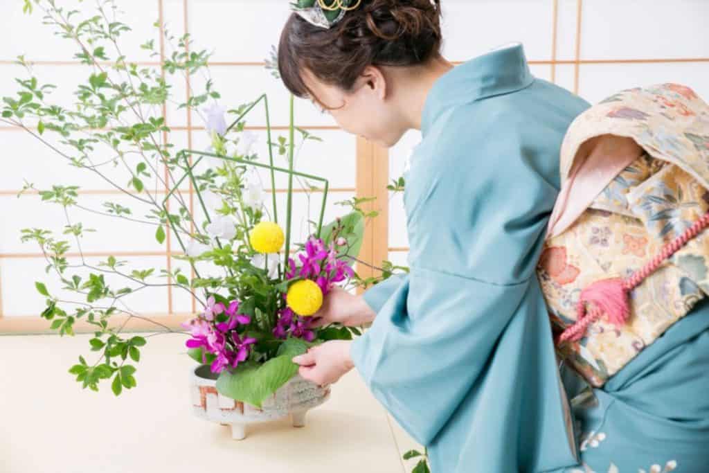 a young woman in blue kimono arranging flowers
