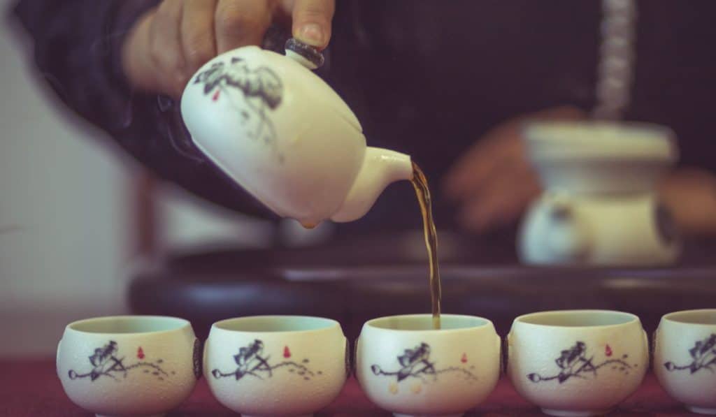 detail shot of man serving Chinese tea into ceramic tea cups.
