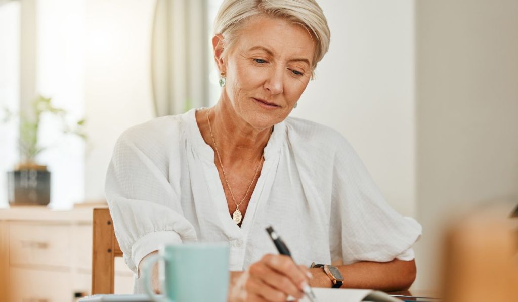 senior woman at a house making notes on notebook paper