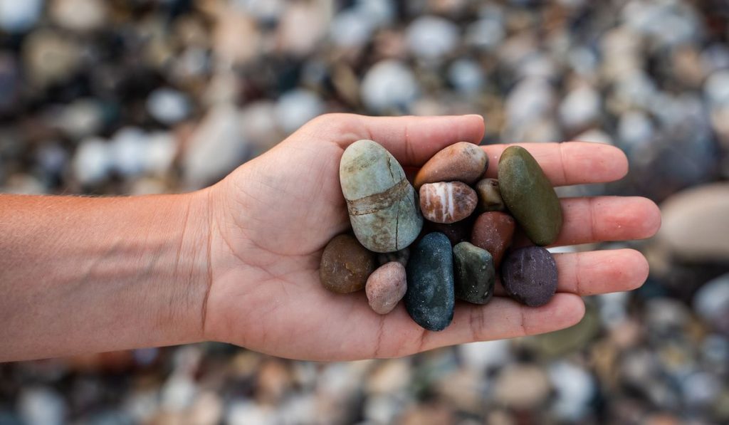Closeup of female hand with heap of pebbles on shingle beach
