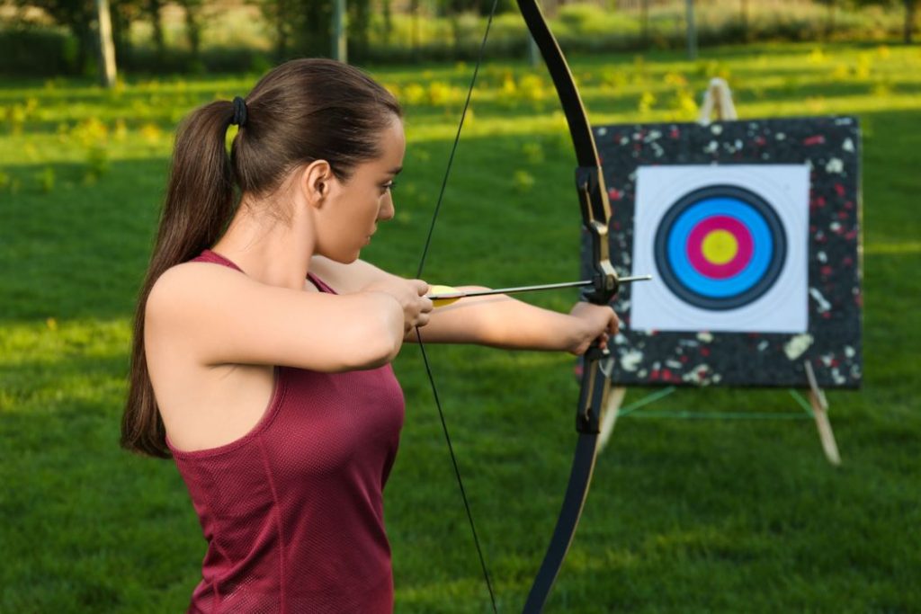 Woman with bow and arrow aiming at archery target in park
